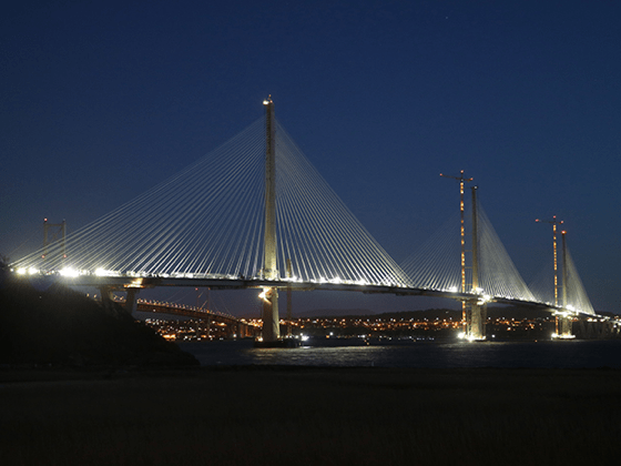 Night time view of an illuminated Edinburgh bridge with city lights in the background.
